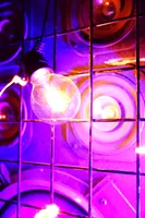 A lightbulb in front of a speaker.
The speaker is protected by a coarse grid of metal wires and lit in bisexual lighting.