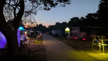 Early morning view down the main road through the general camping area.
We can see differently colored lights along the path as well as
a graffiti covered container with 'freelove' written on it.
The sun is starting to rise on the horizon.