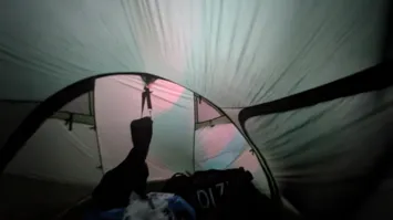 View from inside the tent.
We can see a trans flag casting is colors
onto the tent wall as the morning light filters through it.
The silhouette of a guitar bag visible against the tent wall.